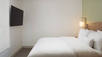Habitación de hotel con una cama, un televisor de pantalla plana en la pared, una lámpara de noche y suelo cubierto de alfombra.