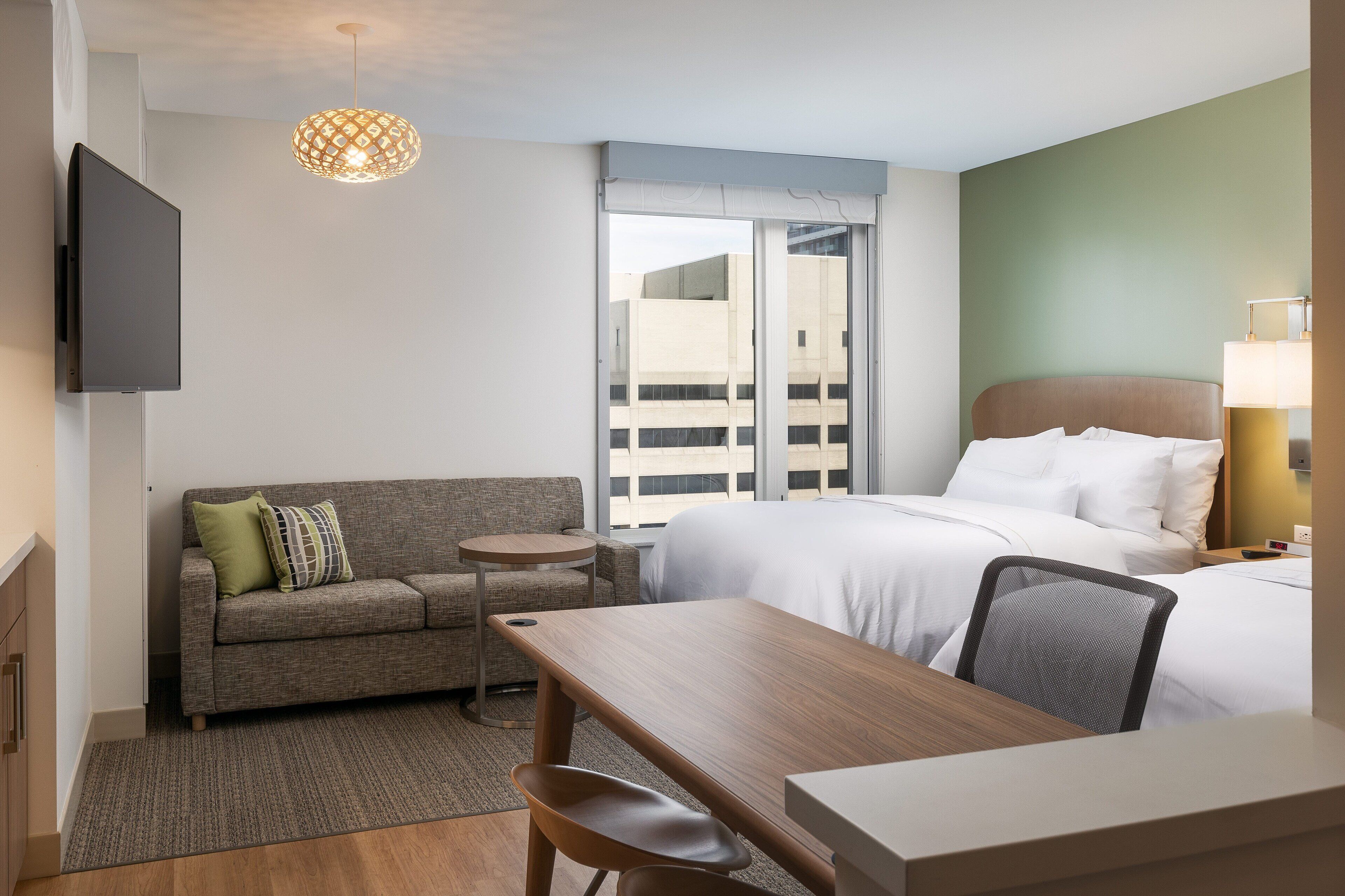 A hotel room with a bed, a sofa, a small table, a chair, a TV, and a lamp.