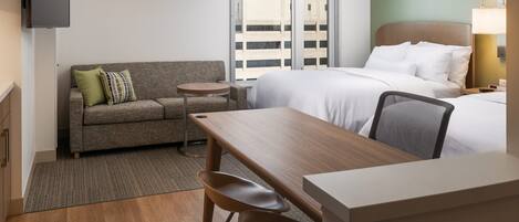 Une chambre d’hôtel avec un lit, un canapé, une petite table, une chaise, une télévision et une lampe.