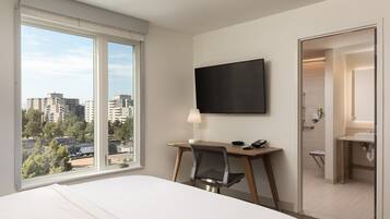 Habitación de hotel con cama, escritorio, silla, televisor y vista a la ciudad.