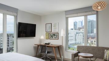 Habitación de hotel con cama, escritorio y silla, sofá, una mesita, lámpara de pie y televisor en la pared.