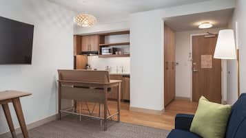 Ein kompakter Wohnbereich mit Küchenzeile, einem Essbereich mit Tisch und Stühlen, einem Sofa mit Kissen und einem an der Wand befestigten Fernseher.