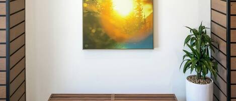 A modern interior with a wooden bench, a framed painting of a forest scene, and a potted plant.