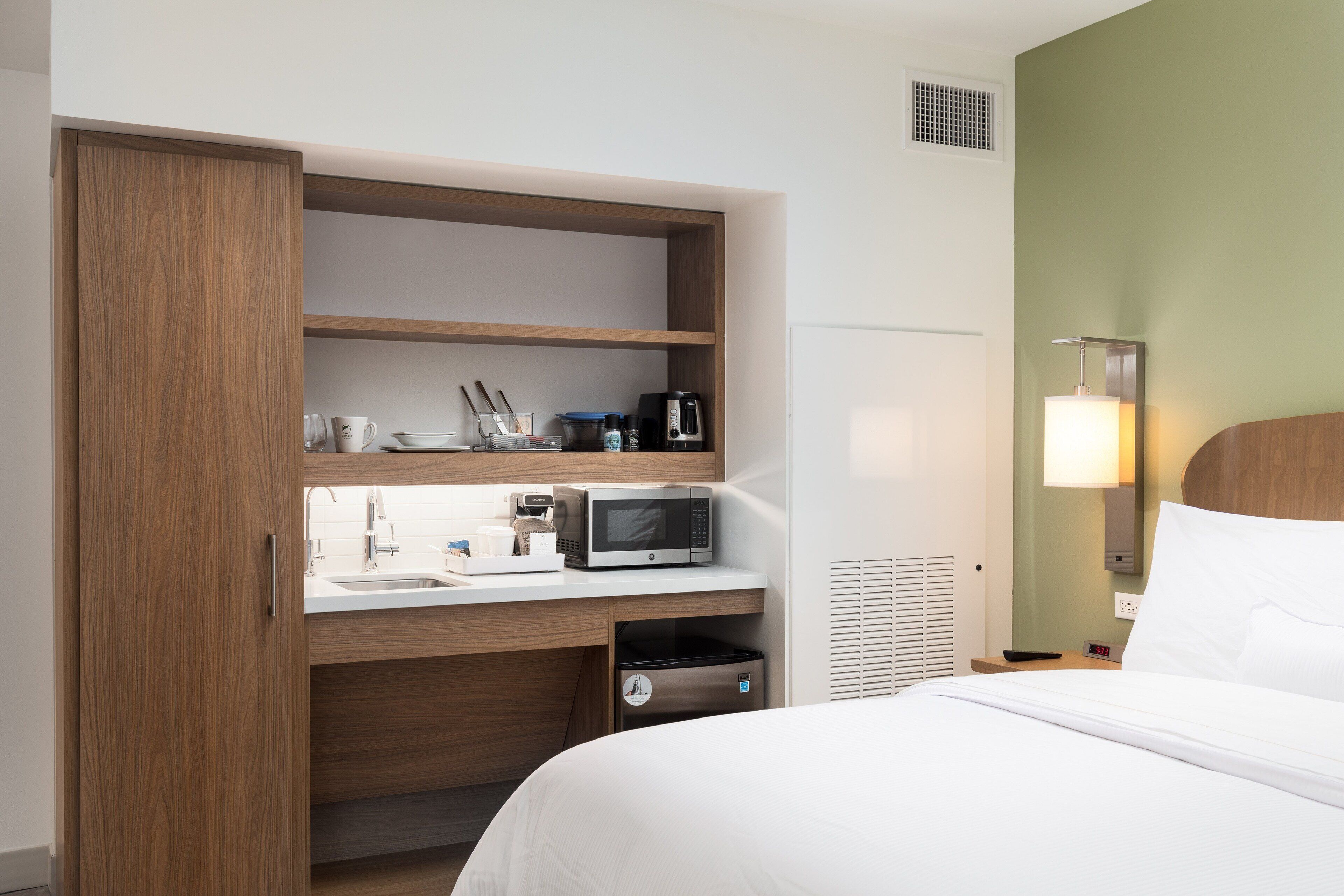 A hotel room with a bed, a desk with a microwave, a coffee maker, and a trash bin.