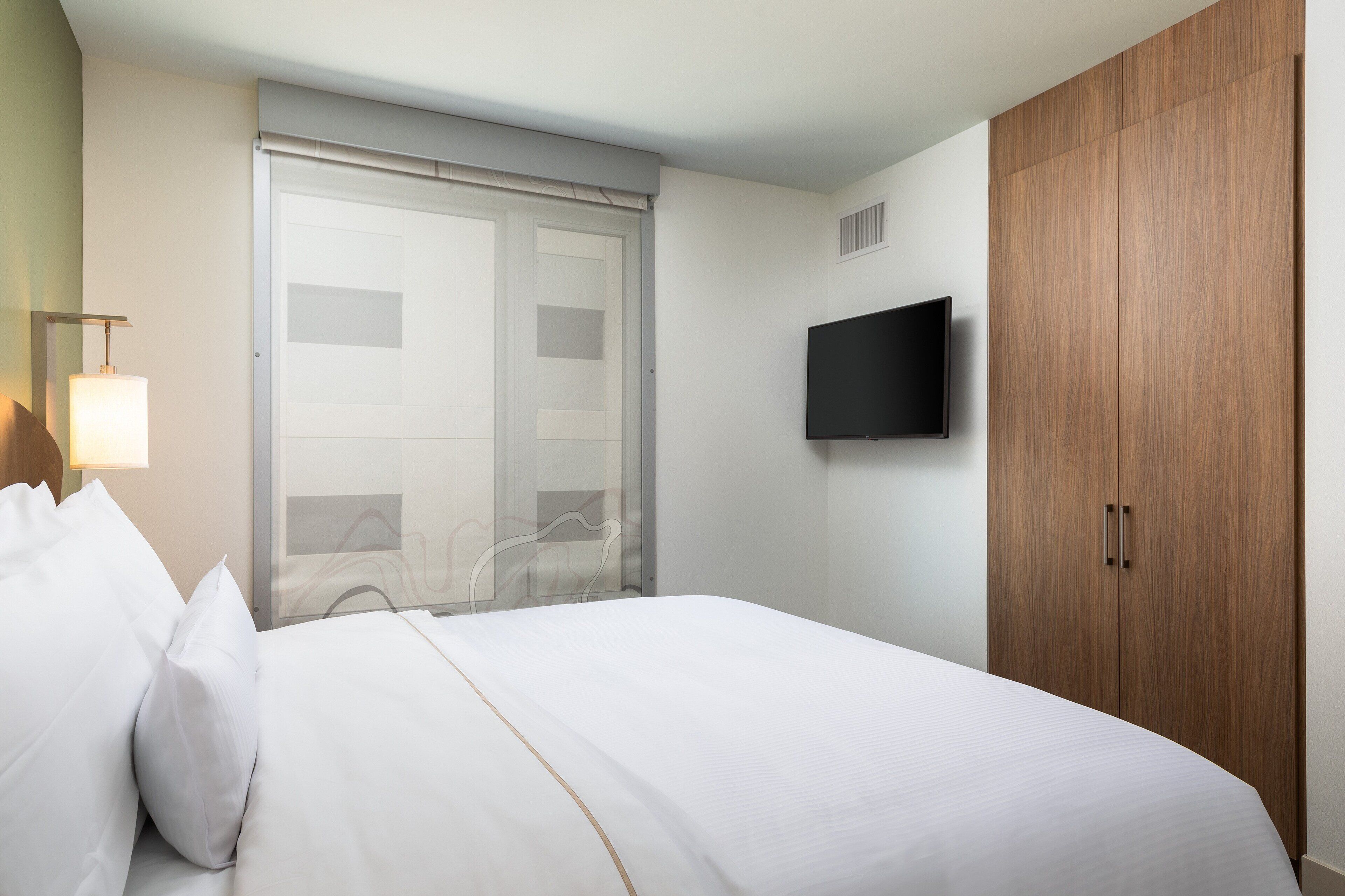 Una habitación de hotel con una cama, un televisor montado en la pared y un armario de madera.