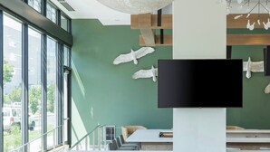 Una sala de estar moderna con un ventanal grande, un sofá gris, un televisor de pantalla plana y una lámpara de techo original.