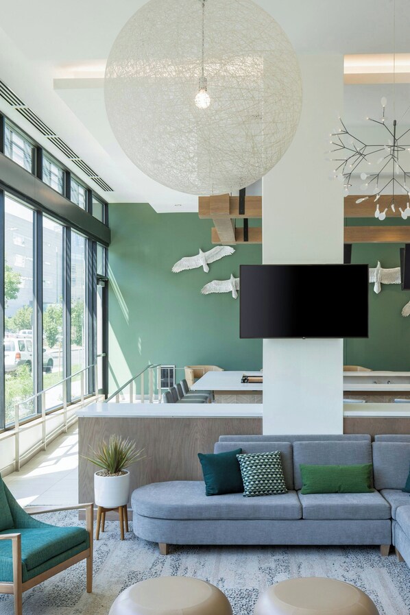 A modern living room with a large window, a grey sofa, a flat-screen TV, and a unique ceiling light fixture. - Element by Marriott Denver Downtown East (Denver)
