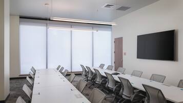 Un salón de conferencias con una larga mesa, sillas, un televisor de pantalla plana y ventanas amplias.
