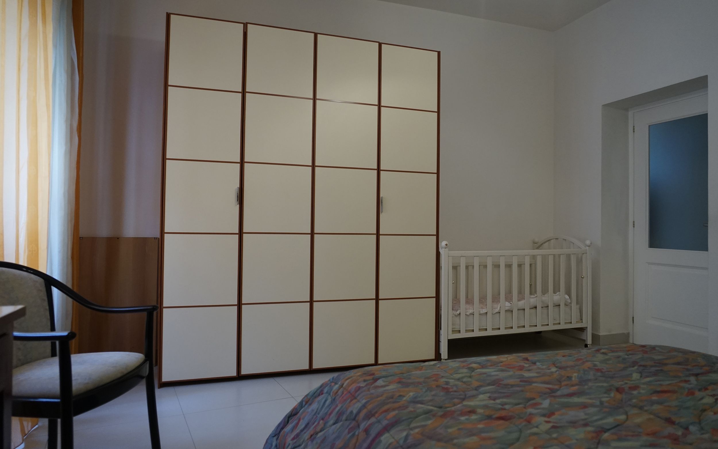 Ein Schlafzimmer mit Bett, Babybett, Stuhl und Kleiderschrank.