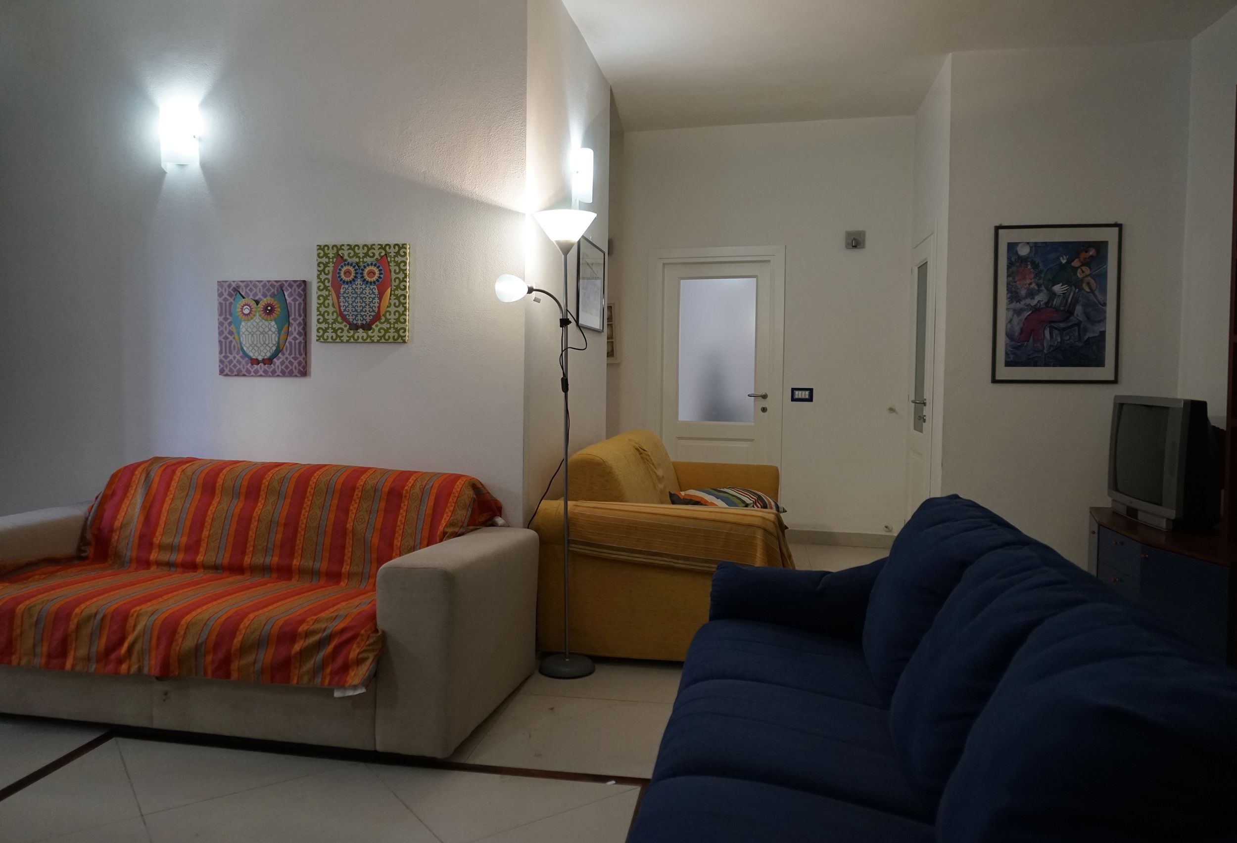 Ein Wohnzimmer mit einer Couch, einem Sessel, einem Fernseher und Kunstwerken an den Wänden.