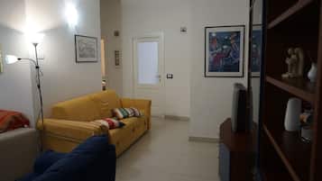 Uma sala de estar com um sofá amarelo, um sofá azul, um abajur e uma estante com objetos decorativos.