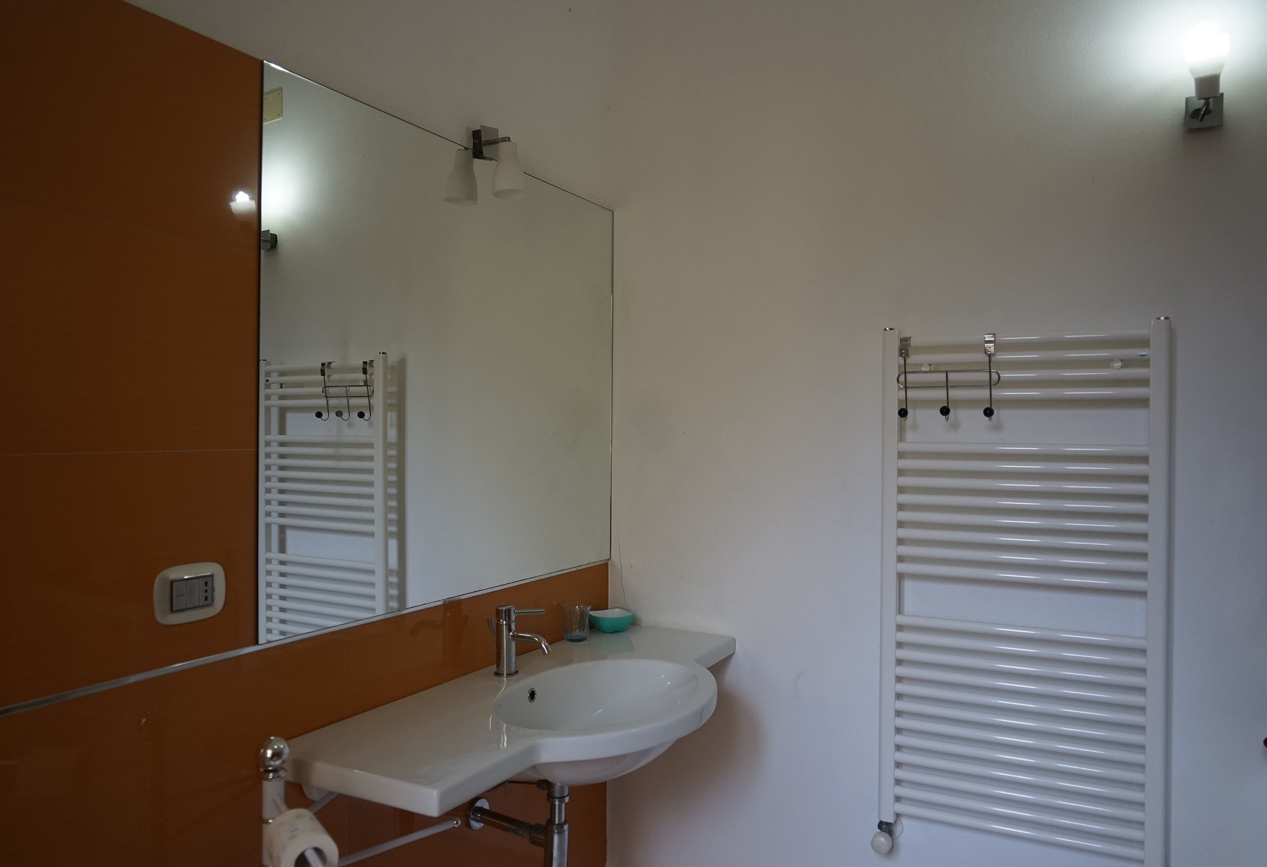 A bathroom with a white sink, a mirror, a towel rack, and a towel warmer.