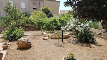 Um jardim com um canteiro de flores circular, diversas plantas e uma grande rocha.