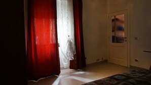 Een kamer met een bed, een deur en een raam met rode gordijnen.