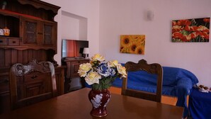 Een eethoek met een houten tafel, stoelen, een bloevas, een televisie en een schilderij aan de muur.