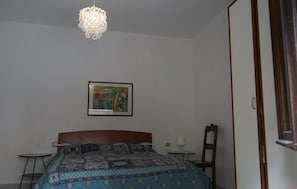 A bedroom with a bed, a framed picture on the wall, a small table, and a chair. - Casa Paguro (Alghero)