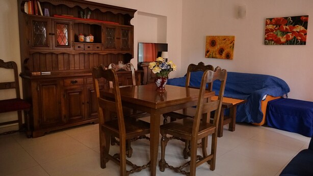 Een eethoek met een houten tafel en stoelen, een kast met glazen deuren en een blauwe bank.