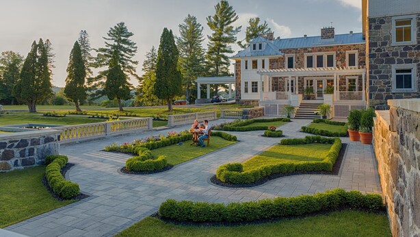 A large stone building with a covered porch and a well-maintained garden with hedges and a pathway. - StoneHaven Le Manoir Relais & Châteaux (Sainte-Agathe-des-Monts)