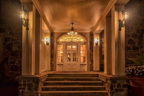 A stone-floored entrance with a grand staircase leading to a door with glass panels. - StoneHaven Le Manoir Relais & Châteaux (Sainte-Agathe-des-Monts)