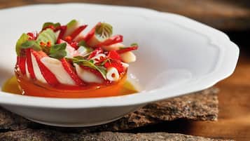 Un plato blanco con un guiso a base de tomate, adornado con hierbas y rodajas de fruta roja, sobre una superficie de madera.