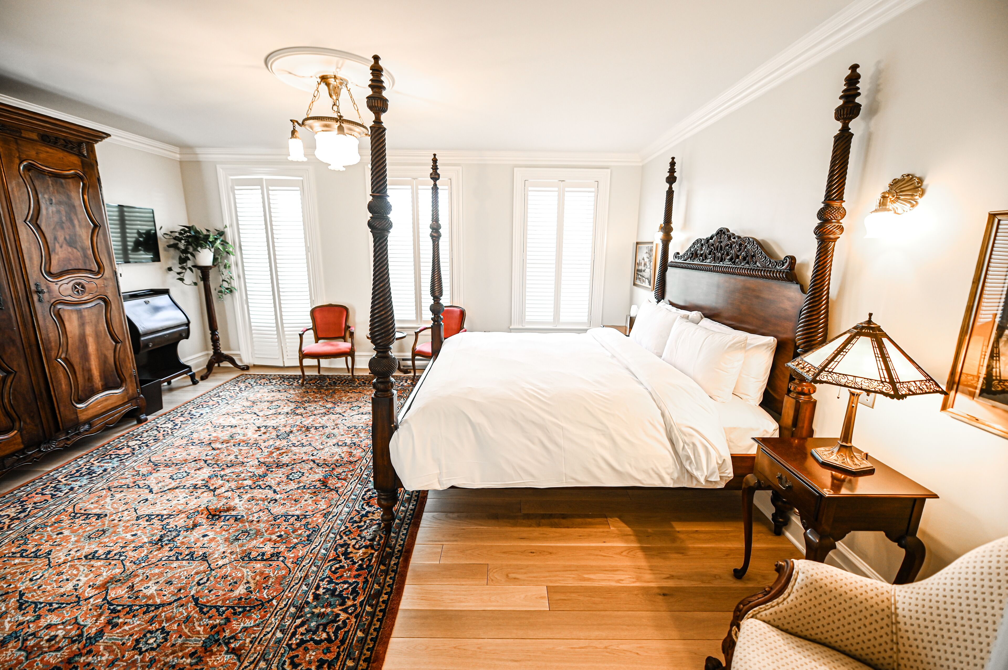 Ein traditionell eingerichtetes Schlafzimmer mit einem Himmelbett, einem großen, verzierten Teppich und einer klassischen Holzkommode.