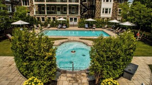 A pool area with lounge chairs and umbrellas, surrounded by greenery and a stone building in the background. - StoneHaven Le Manoir Relais & Châteaux (Sainte-Agathe-des-Monts)