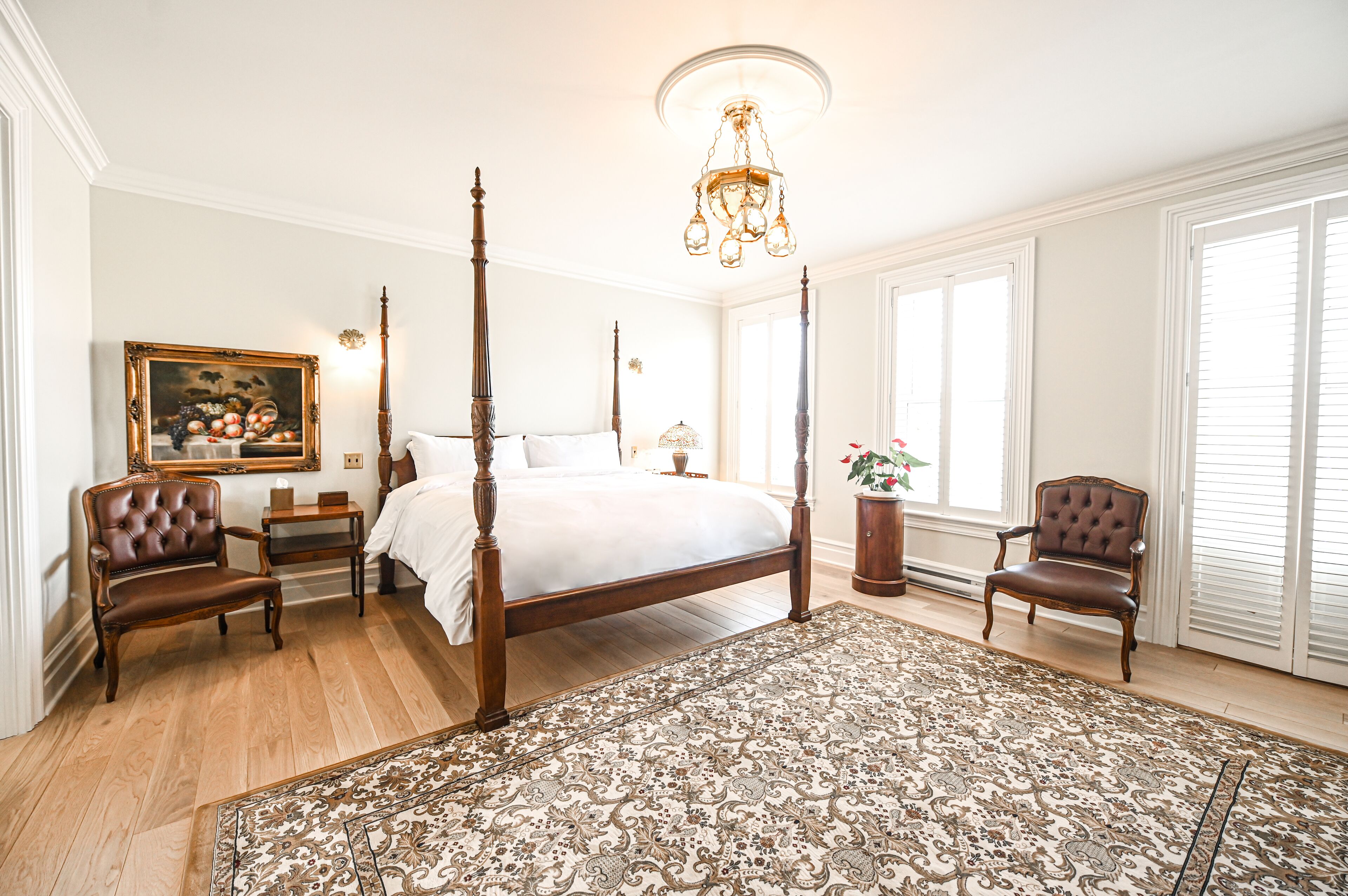 A spacious bedroom with a four-poster bed, a large ornate rug, and classic wooden furniture.