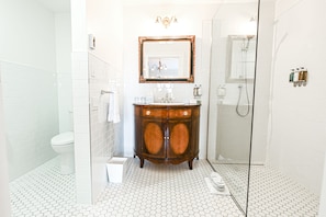 A bathroom with a white tiled floor, a wooden vanity with a mirror, a toilet, and a glass-enclosed shower area. - StoneHaven Le Manoir Relais & Châteaux (Sainte-Agathe-des-Monts)