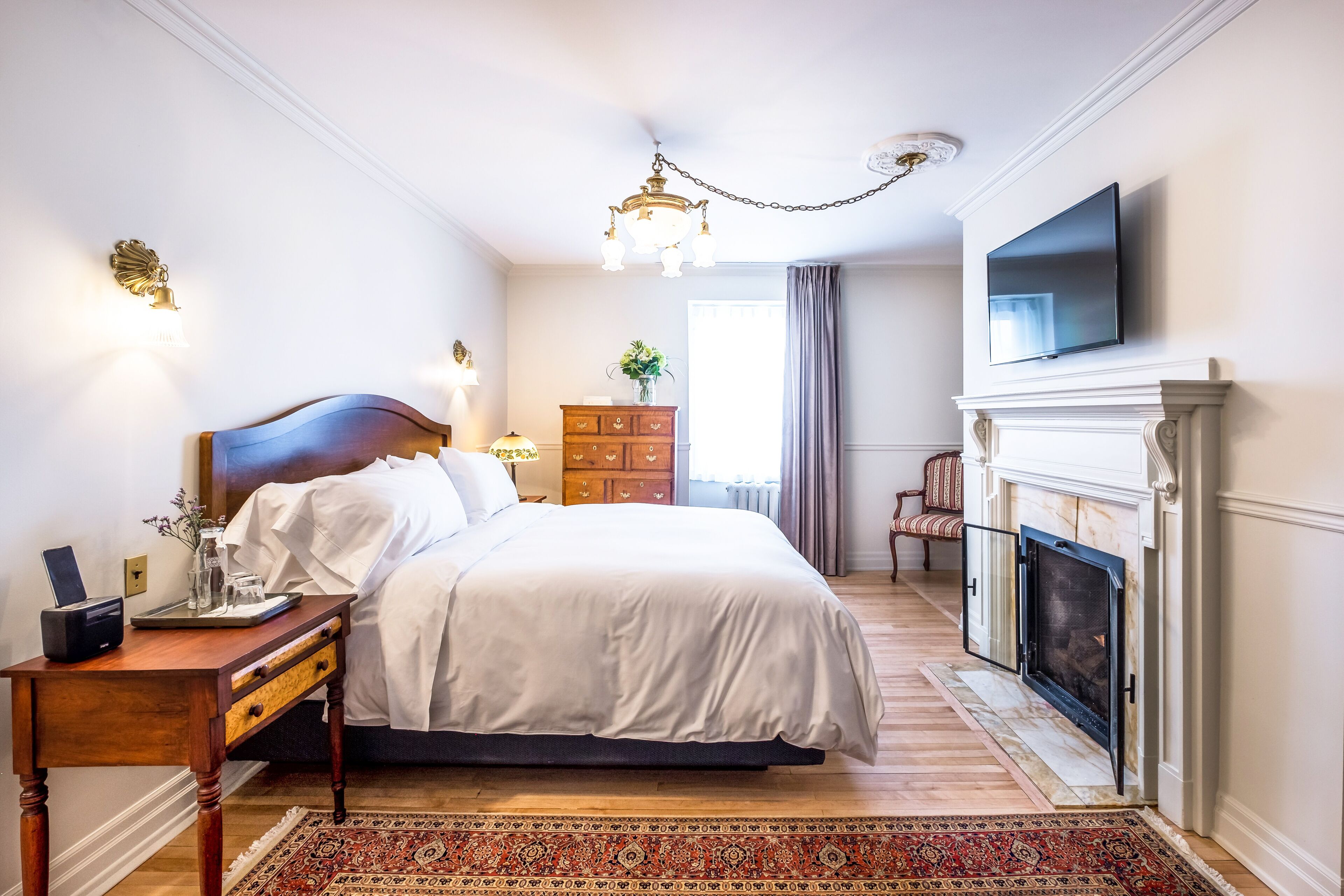 A bedroom with a large bed, a nightstand, a dresser, a fireplace, and a television.