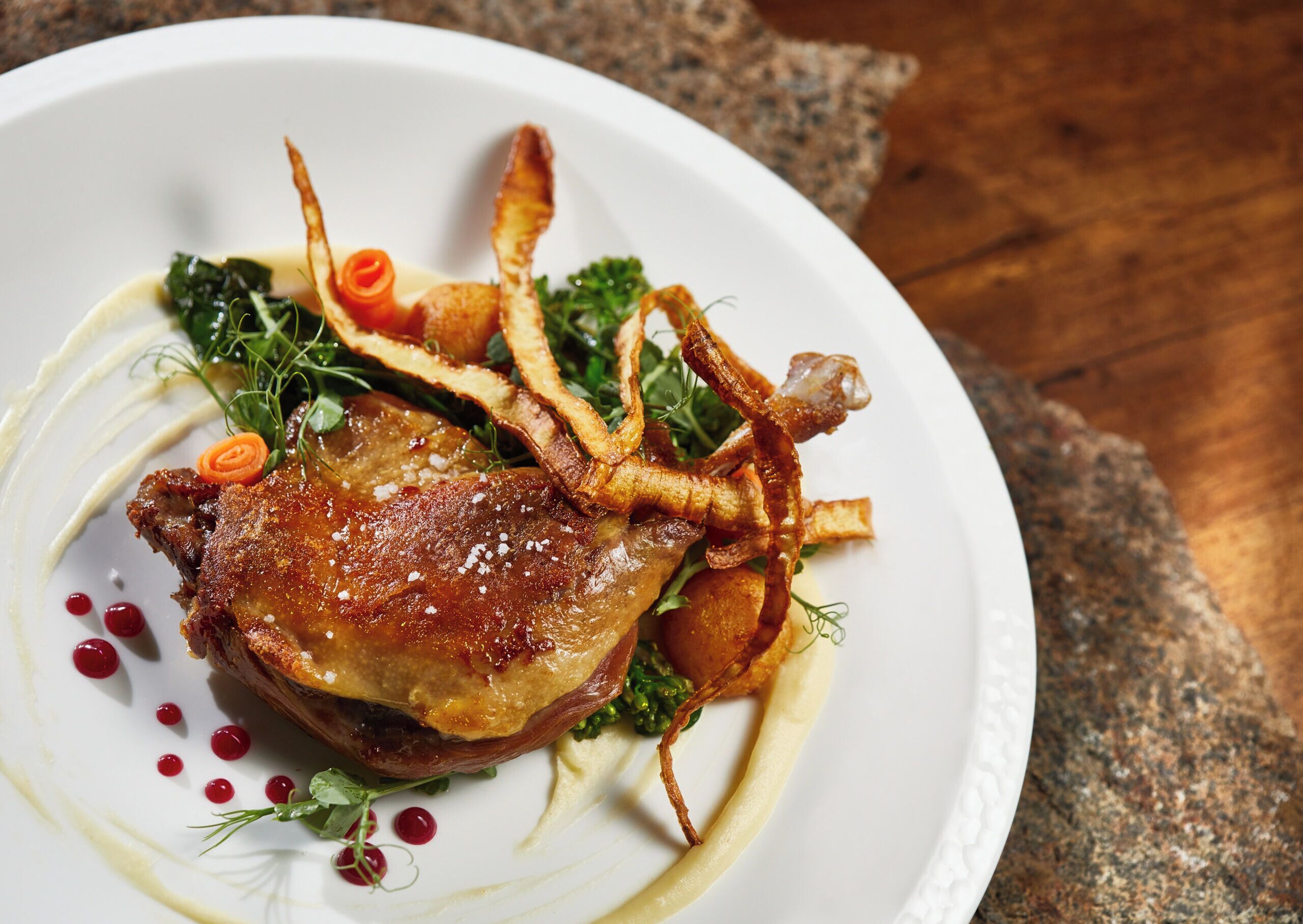 A plate of food with a roasted meat, vegetables, and garnishes.