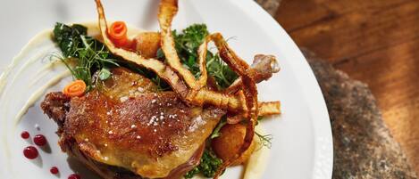A plate of food with a roasted meat, vegetables, and garnishes.