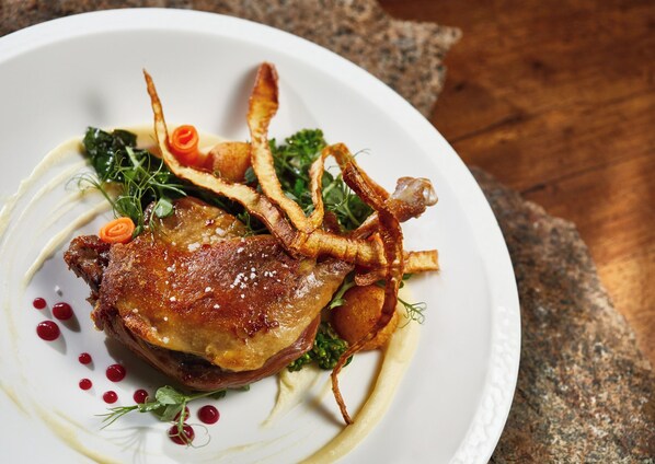 A plate of food with a roasted meat, vegetables, and garnishes.