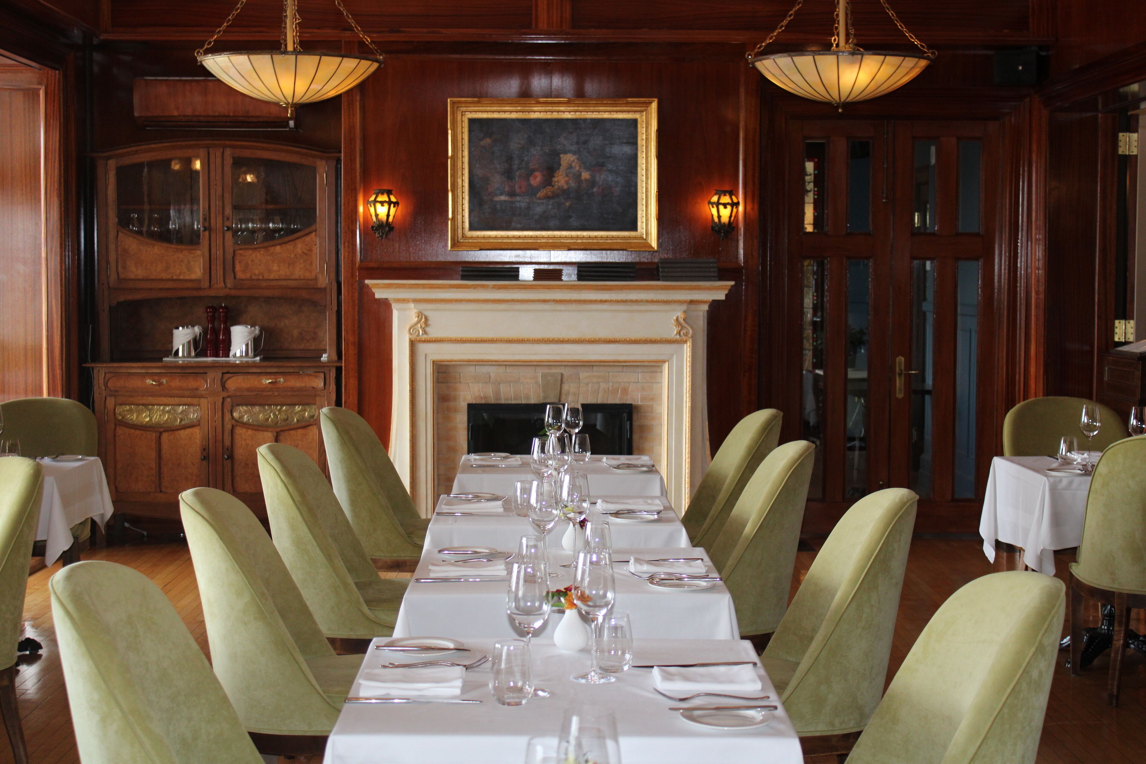 A formal dining room with a long table set for a meal, surrounded by green upholstered chairs.