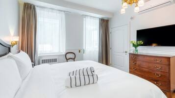 A hotel room with a large bed, a wooden dresser, a flat-screen TV, and a window with curtains.
