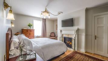 Un dormitorio ordenado con una cama grande, una chimenea, un televisor montado encima y un aparador de madera.