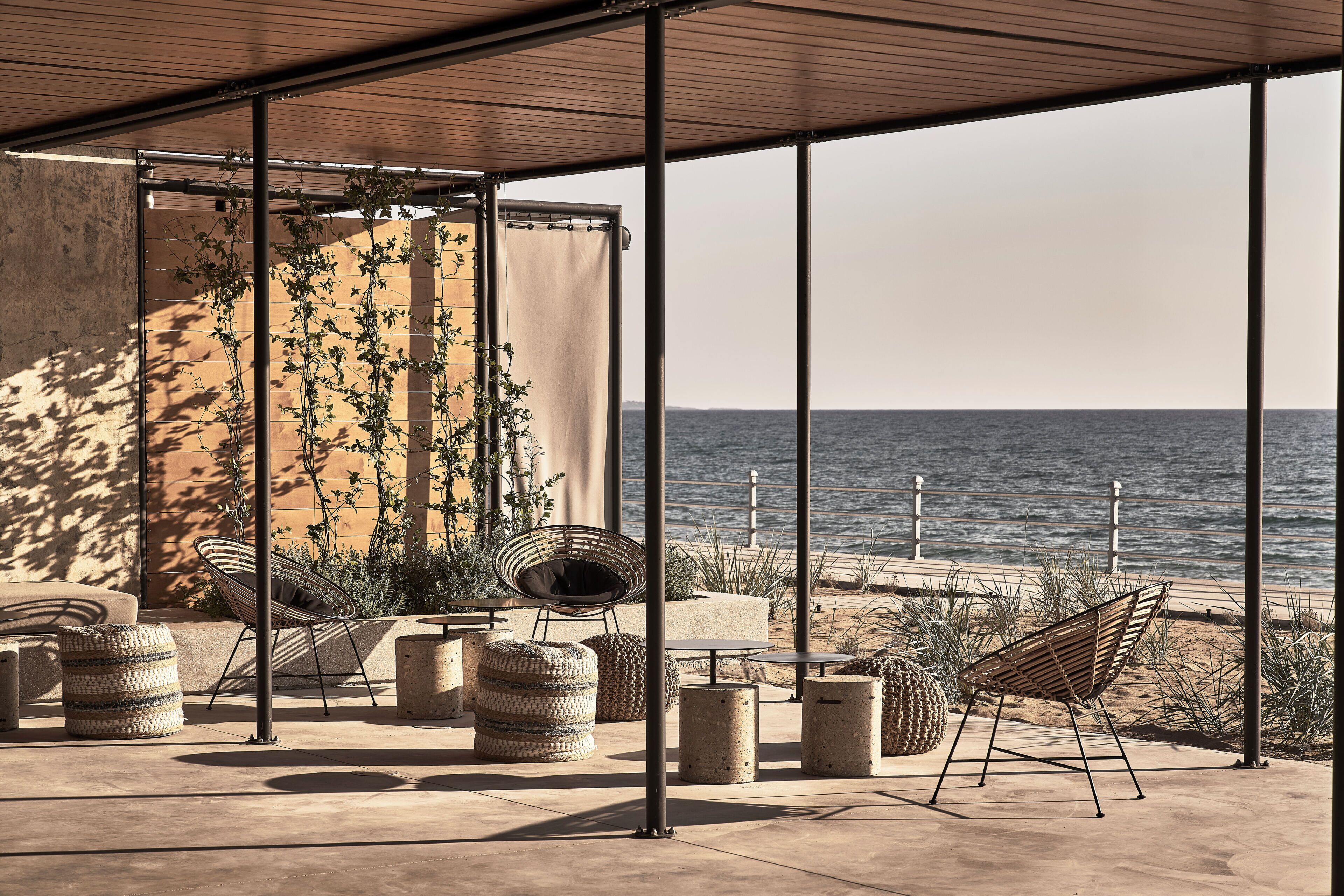 An outdoor seating area with a view of the sea, featuring a covered patio, chairs, and decorative plants.