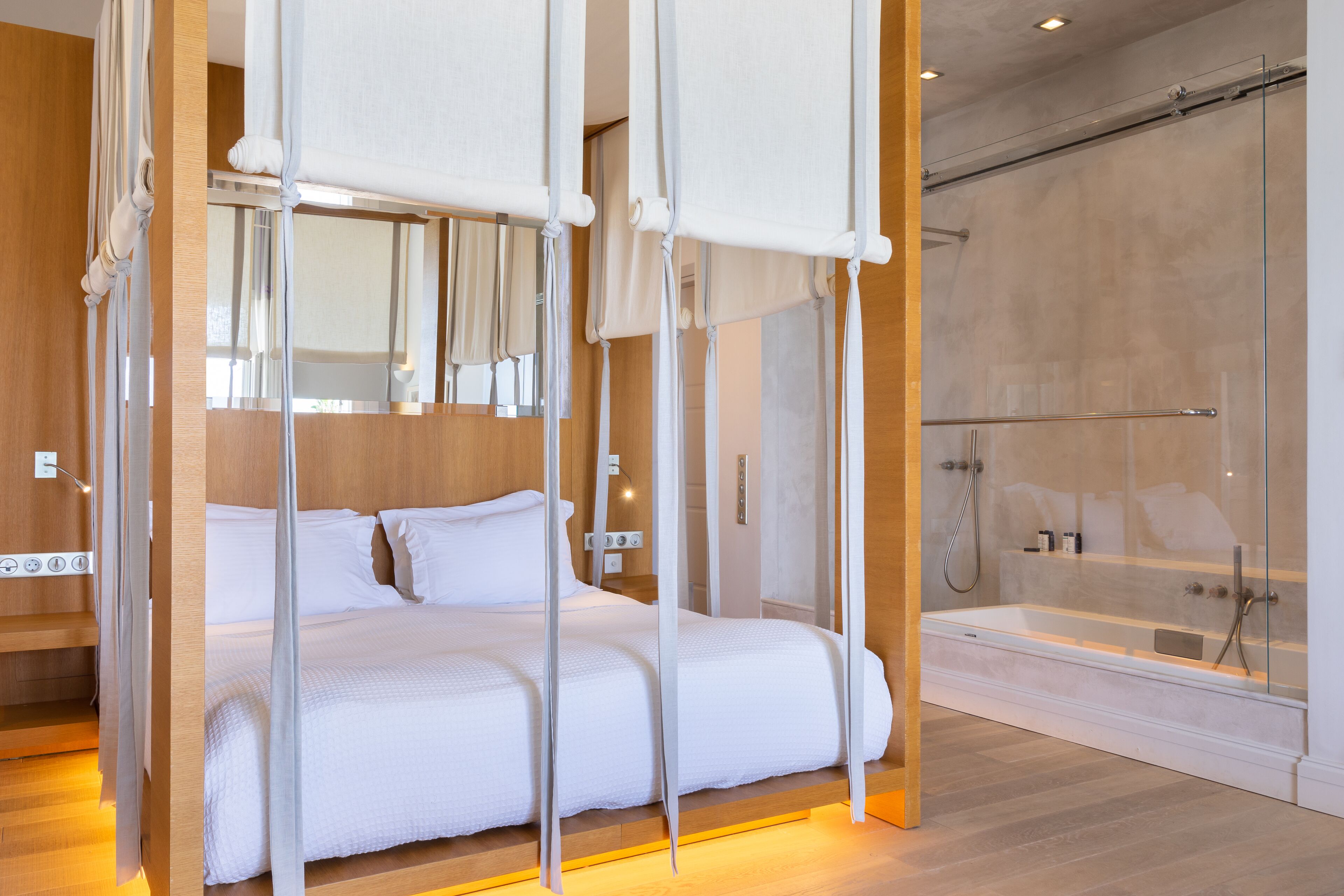 Una camera d'albergo moderna con un letto, una cabina doccia in vetro e un pavimento in legno.