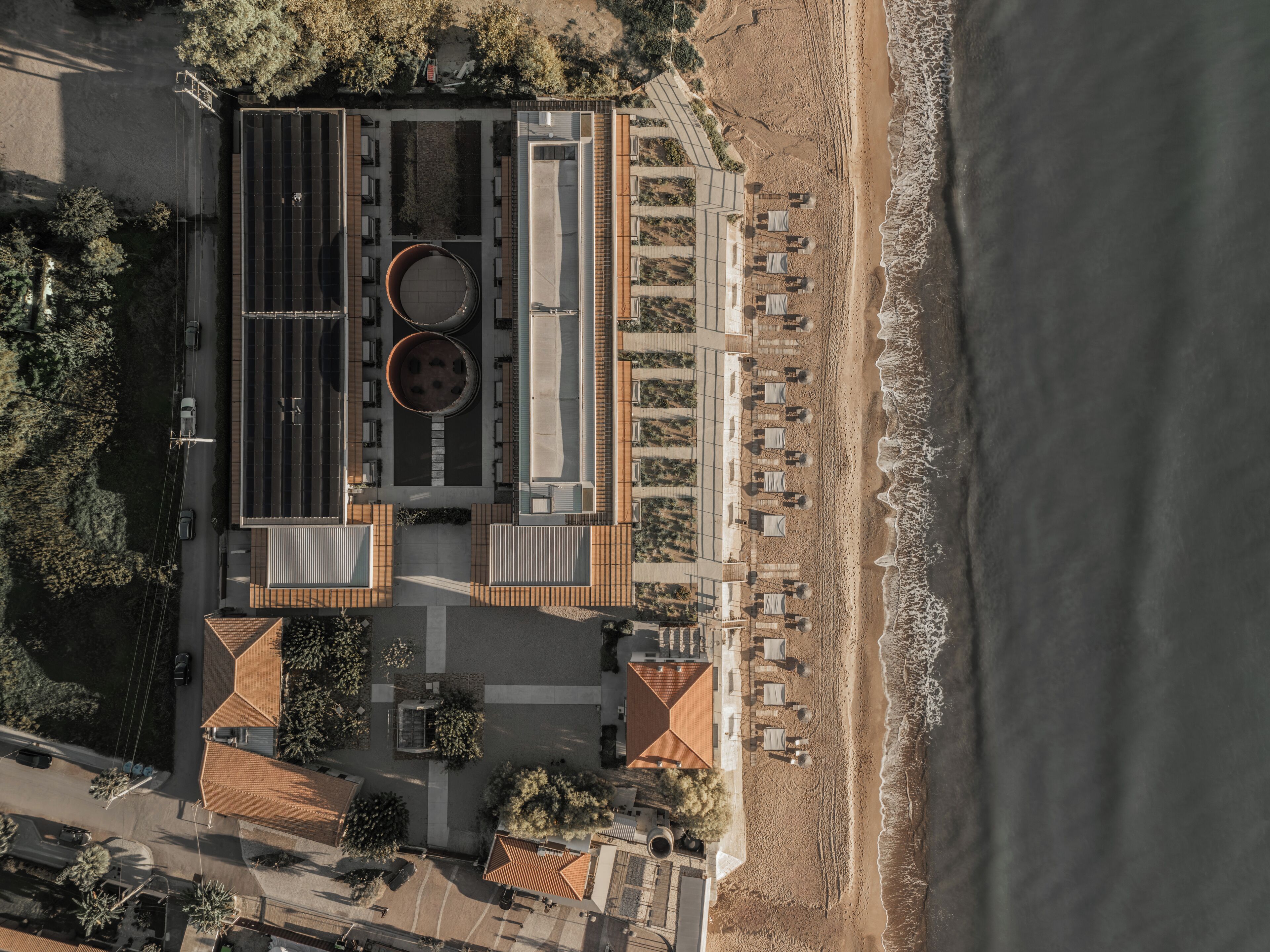 An aerial view of a coastal hotel with a rooftop pool, beachside seating, and a parking area.