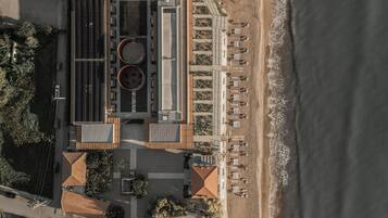 An aerial view of a coastal hotel with a rooftop pool, beachside seating, and a parking area.