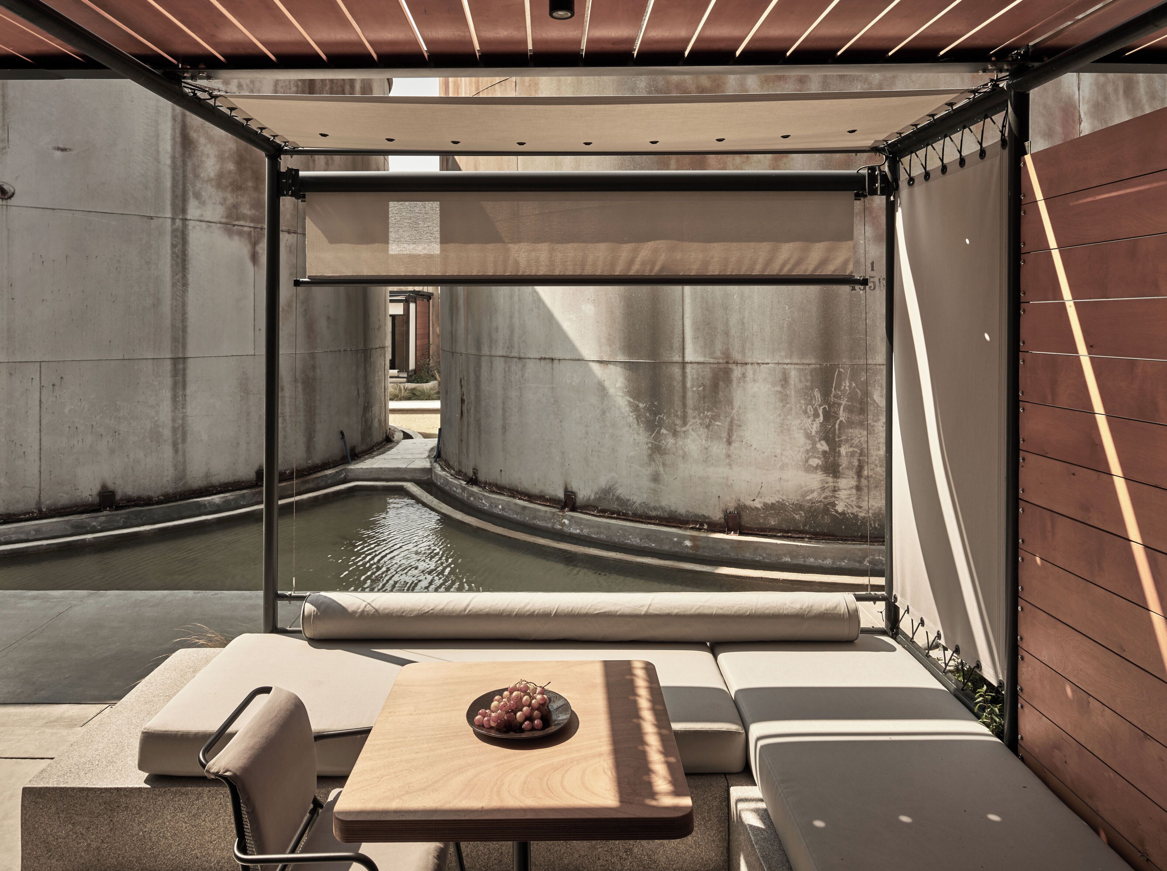 A modern outdoor seating area with a pool, lounge chairs, and a table with a bowl of fruit.