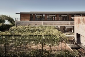 Un edificio moderno con techo plano y grandes ventanales, rodeado de un jardín con diversas plantas.