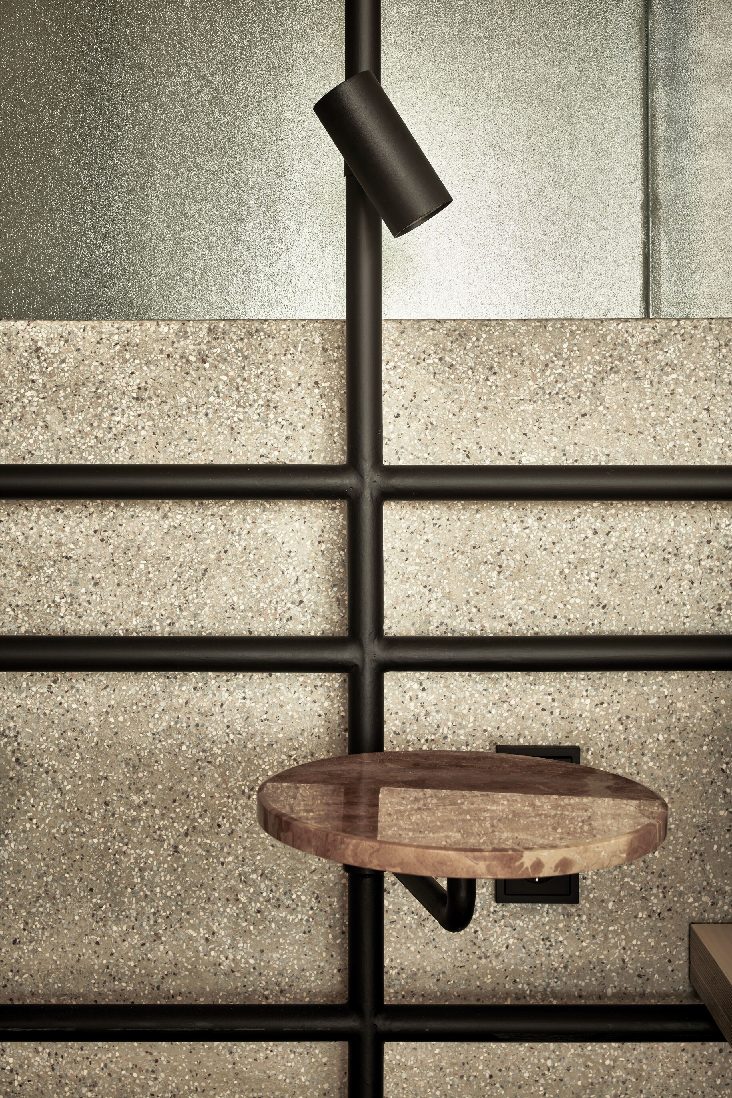 En modern inredning med ett terrazzogolv, ett träbord och en svart metallstång med en lampa.