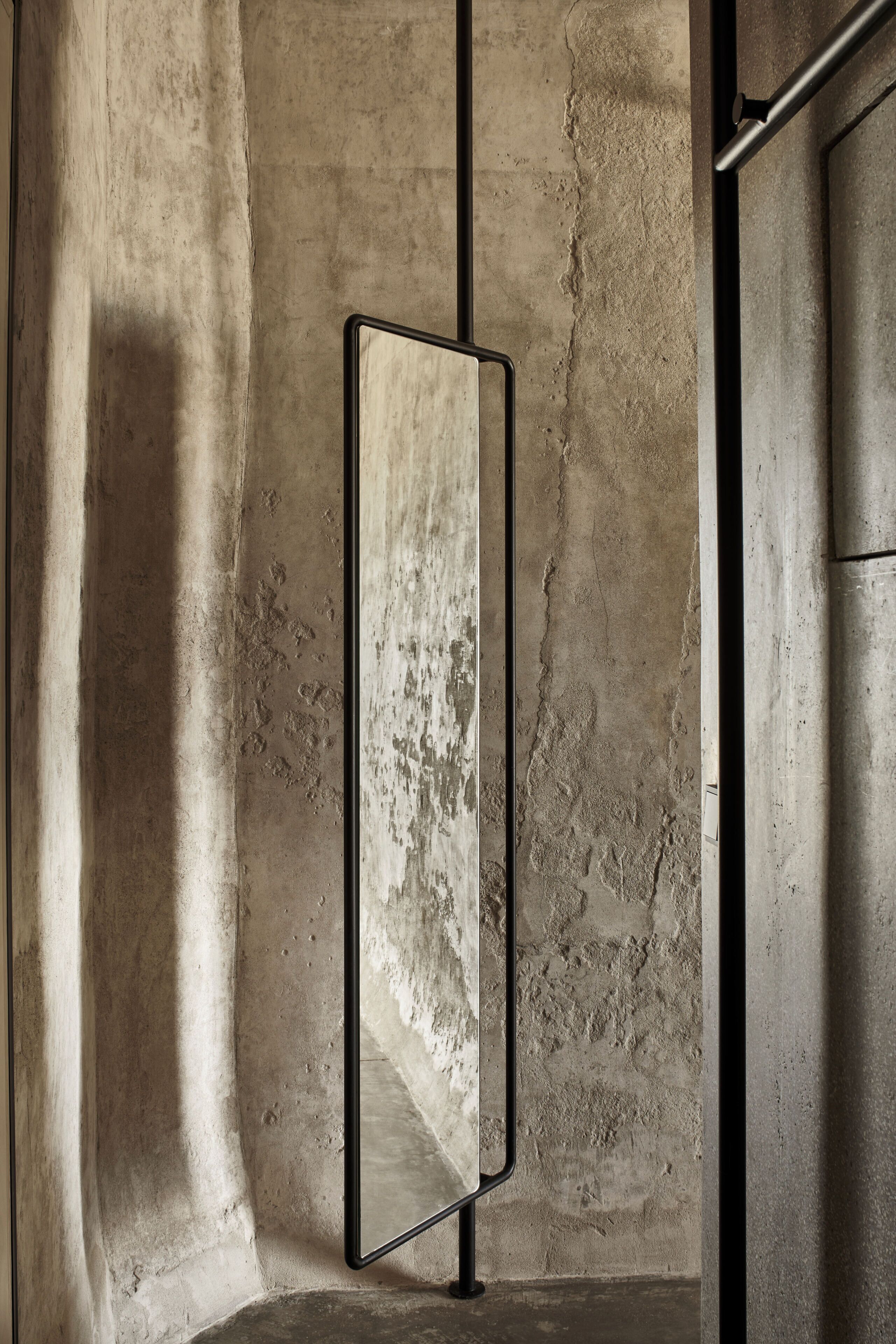A mirror with a black frame mounted on a textured wall.
