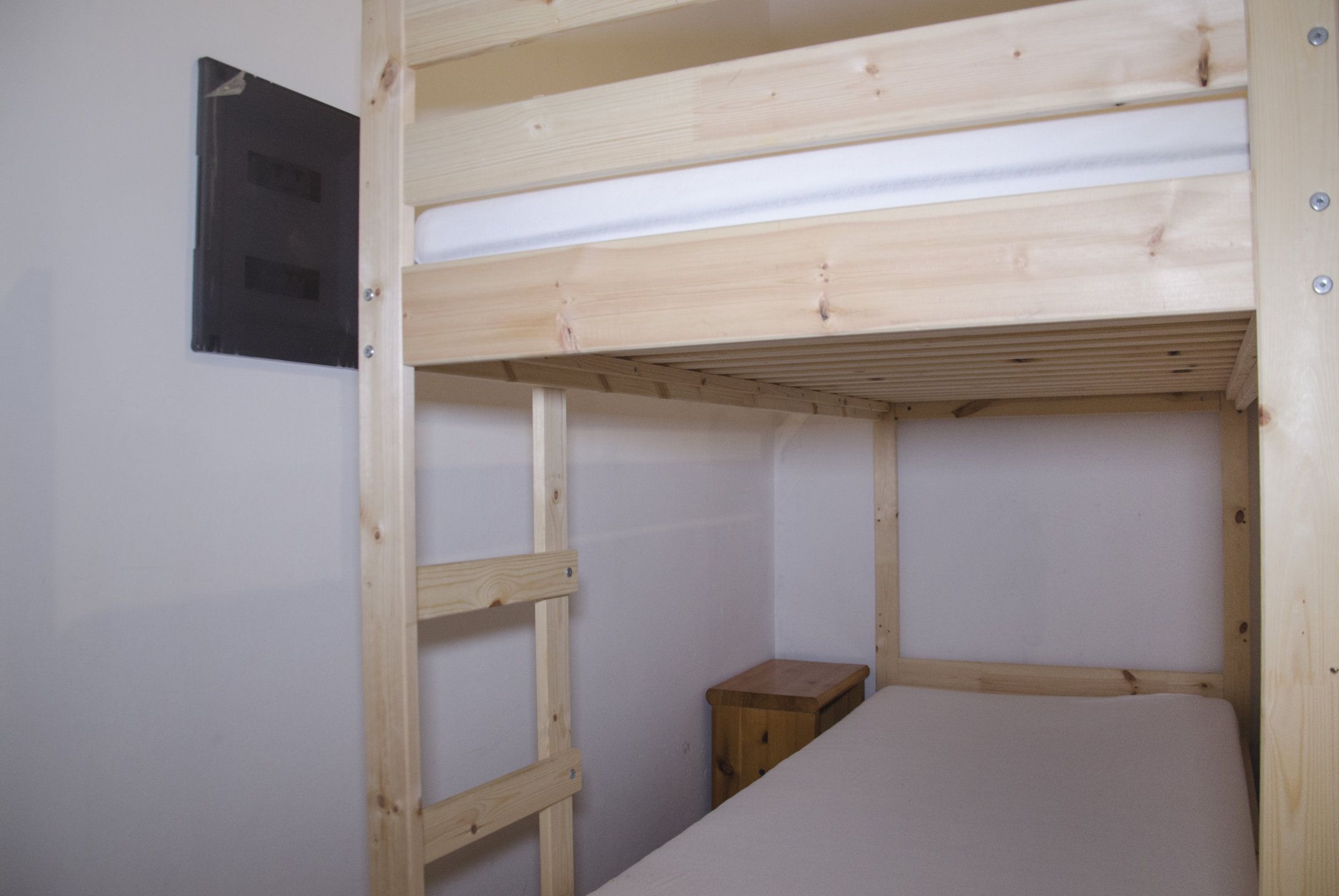A bunk bed with a wooden frame and a small wooden nightstand beside it.