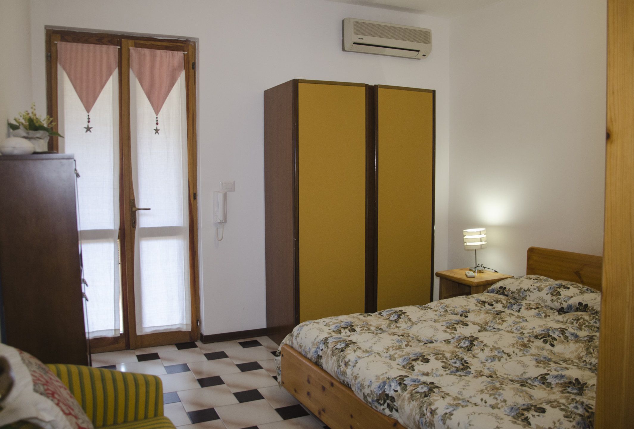 A bedroom with a bed, a wardrobe, a chair, a lamp, and a door with curtains.