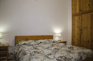 A bedroom with a wooden bed, two bedside tables, and a wooden wardrobe. - Casa Sparaglione (Alghero)