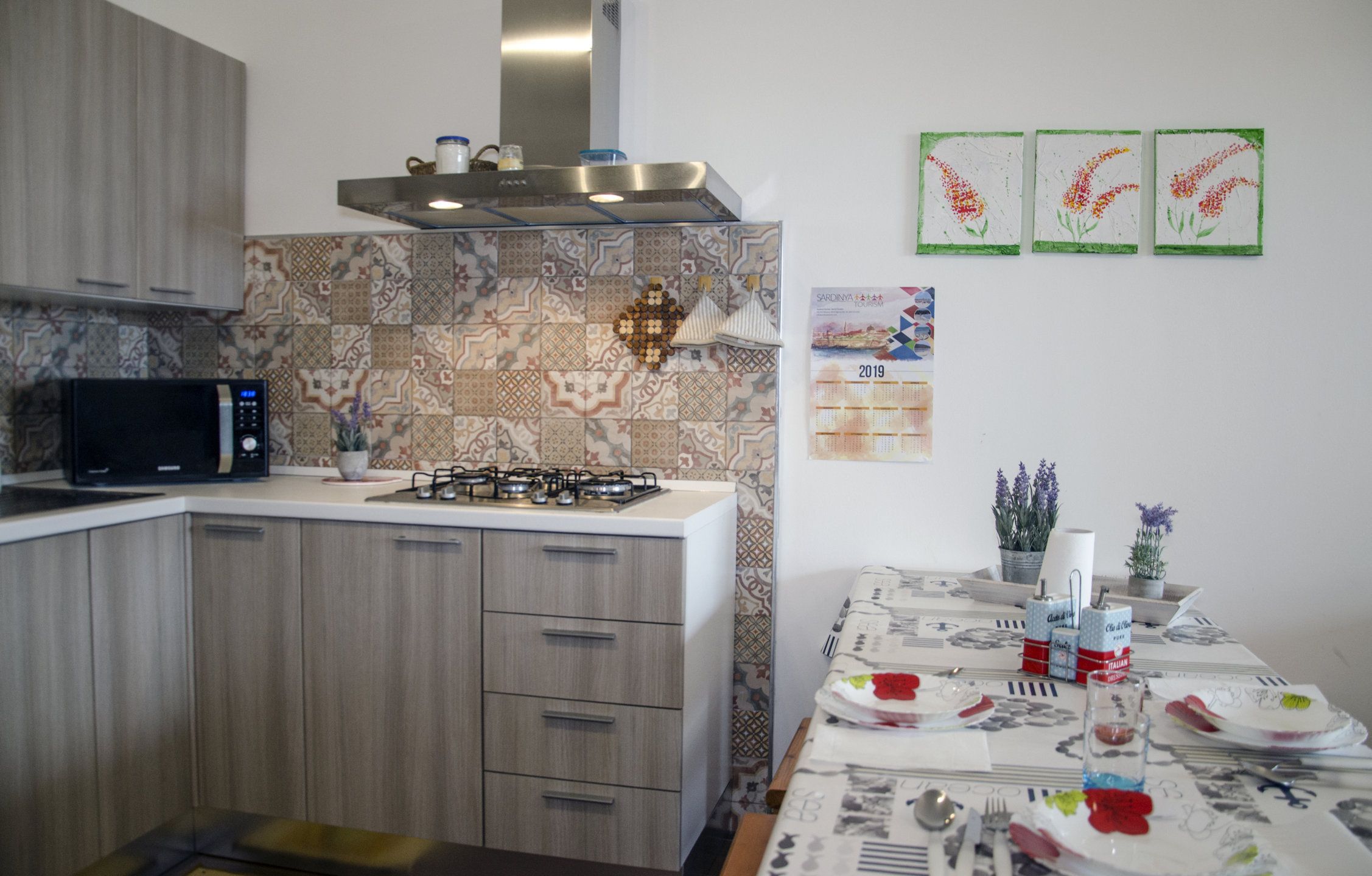 Une cuisine moderne équipée d’un four à micro-ondes, d’une cuisinière et de meubles en bois. Un calendrier est accroché au mur et une table est dressée pour le repas.