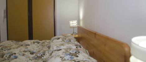 A bedroom with a wooden headboard, a bed with floral bedding, a nightstand with a lamp, and a wardrobe with a mirror.