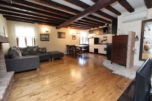 Uma sala ampla com piso de madeira, um sofá, uma mesa de jantar e uma cozinha ao fundo.