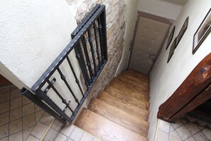 Uma escadaria de madeira com guarda-corpo de metal preto, que leva a um quarto com porta branca e piso de azulejos.